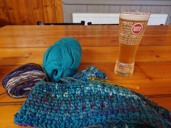 Crocheting a blanket with two sock yarn strands held together, in a restaurant and enjoying beer