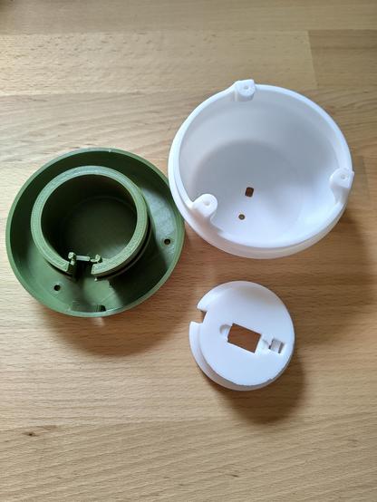 Einzelteile der Glowlight-Lampe aus 3D-Druck. Zu sehen sind das grüne Innengehäuse, ein weißes Außengehäuse und eine weiße Abdeckung mit Aussparungen für die Elektronik.