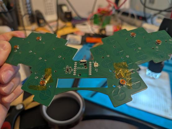 Back of a green small keyboard PCB showing some kapton tape securing two small magnet wire bodges.