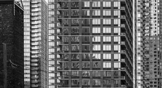 A black-and-white image showing parts of multiple city buildings overlapping one another in compressed perspective.  There are different repeating patterns (windows, bricks et al).