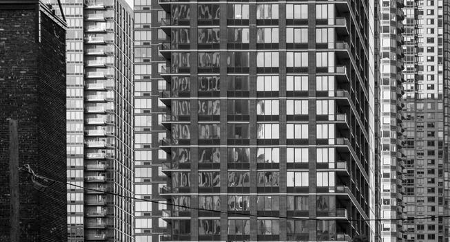 A black-and-white image showing parts of multiple city buildings overlapping one another in compressed perspective.  There are different repeating patterns (windows, bricks et al) each in their own areas.