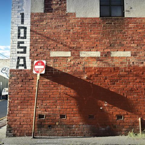 A brick wall of an old building. The morning sun casts a long shadow from a No Entry sign on the left, across the wall. On the top right corner is a blocky hand-painted “105A”.