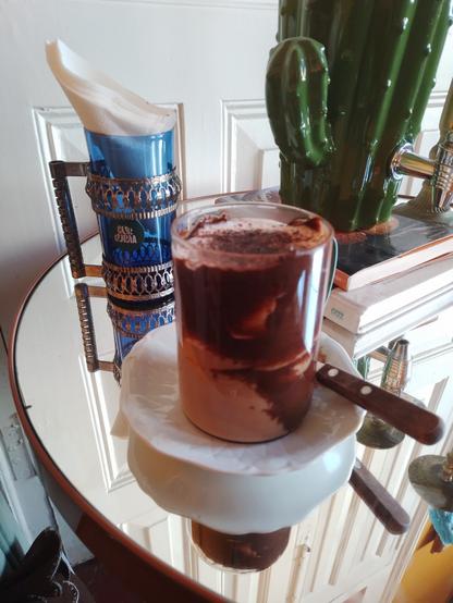 A cup of a delicious mocaccino, in a table made of a mirror, with a cactus on the side.