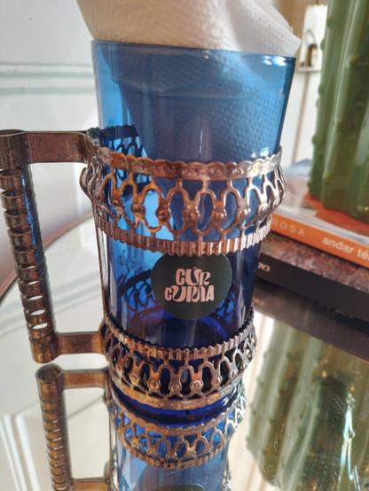 An old cup, made of blue glass, and adorned with bronze-like metal.