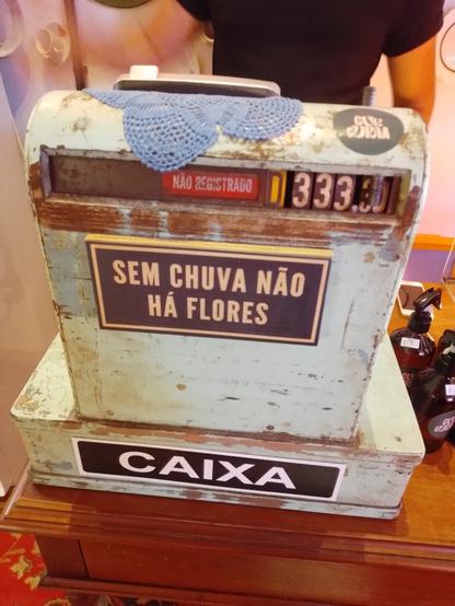 An old and rusted cash register, with a modern sticker saying: "without rain, you don't have flowers"