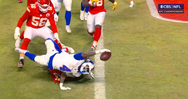 Buffalo Bills receiver, James Cook, with his whole body horizontal, airborne, and twisting out of reach of two Kansas City defense-men, as he reaches one arm at maximum extension placing his hand across the goal line to get the entire football over the line and secure a touchdown for the Bills