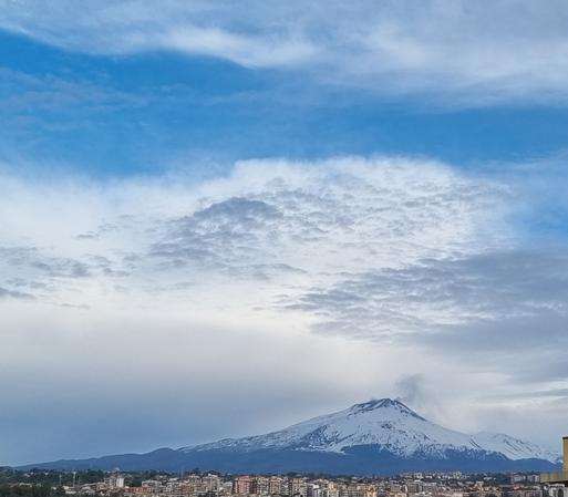 Etna innevato, mentre nel cielo azzurro passano sopra nuvole bianche che sembrano cariche di altra morbida neve