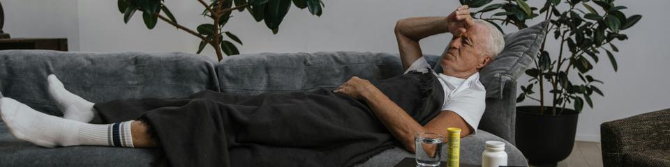 Ein Mann liegt krank auf einer Couch - Sinnbild für den hohen Krankenstand in Deutschland