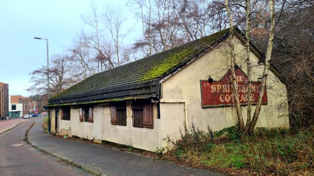 A low, single-storey, abandoned pub building at the side of a Glaagow Road
