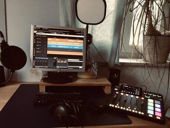 Ein Bildschirm mit den Hüllkurven einer Aufioaufnahme und Linux-UI, ein Mikrofon mit Popschutz, ein bunt leuchtendes Mischpult. Der Eindruck ist einladend zum Arbeiten.