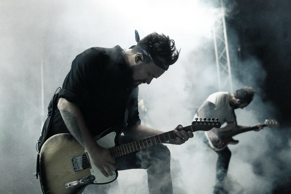 Gitarrist und Bassist rocken auf der Bühne. Künstlicher Nebel und grelles Licht.