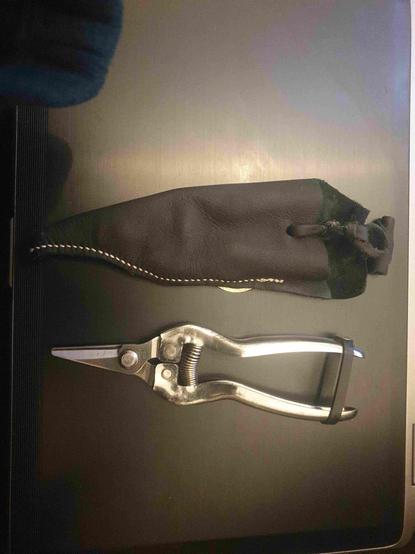 Vendangette, sécateur à vendanges avec contre-lame dentée, chinoise, en inox, de grande qualité.
Housse en cuir automobile de récup noir, faite main, cousue de fil blanc, bouton viking en cuir enroulé.