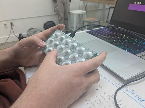 Hands holding a phone-sized box with 18 translucent plastic bubbles on top, reminiscent of bubble wrap.