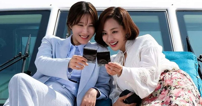 Lee Ji Ah, in a light blue suit & Eugene, in a white top & floral skirt sitting on a yacht looking at polaroid pictures from the 2020 South Korean drama "The Penthouse: War in Life."