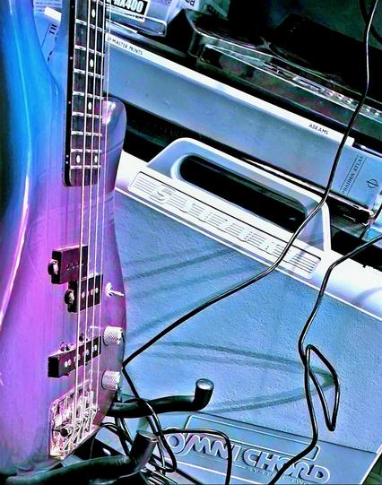 An over-saturated and colour shifted photograph of a bass guitar, Omnichord case, circuit-bent drum machine, and minidisc player box