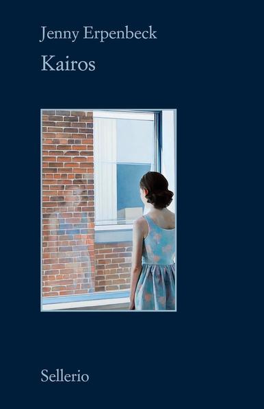 Copertina di "Kairos" di Jenny Erpenbeck con una giovane donna in un abito fantasia in piedi vicino a una finestra, che riflette su un muro di mattoni all'esterno.
