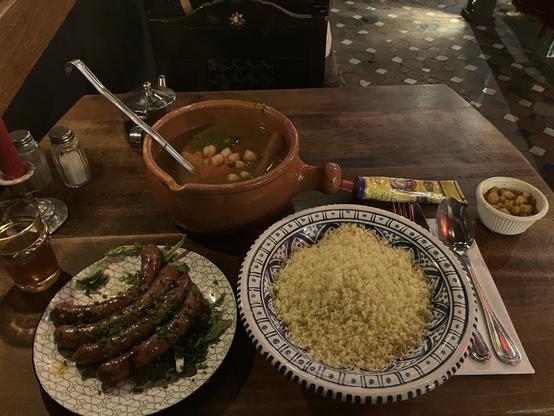 a deep plate with couscous, a terrine with the vegetables and sauce, a plate with Merguez (decorated with at LEAST three different greens, which I ate as well of course), a small dish of marinated raisins, and a tube of Harissa