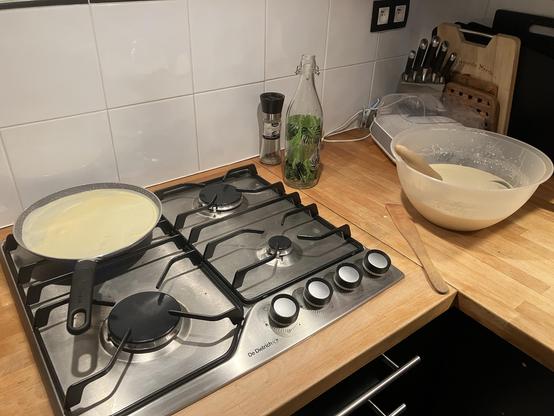 Une plaque de cuisson avec une crêpière et un saladier plein de pâte à crêpe