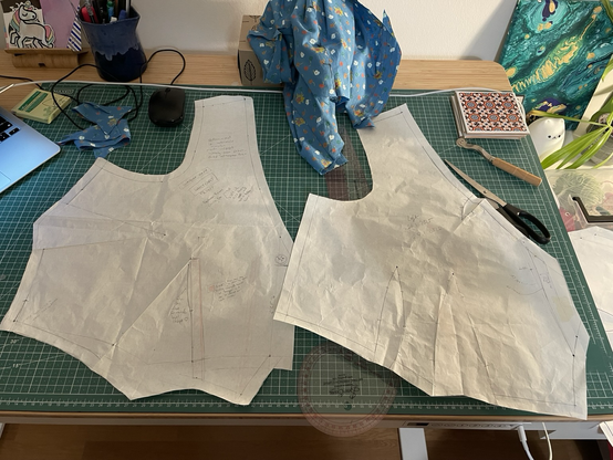 Two waistcoat pattern fronts laid on a cutting mat. The one on the left is the original I drafted, with 1 side dart and 1 waist dart. On the right is the latest pattern, which looks more angular and has two rounded waist darts.