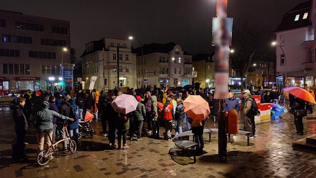 Eine Gruppe von um und bei 100 Demonstrierenden bei Regen. Einige halten Regenschirme.