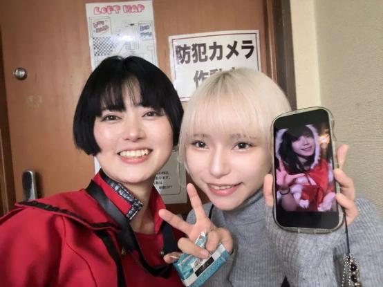Chiyo in red. Sami in white holds up a phone with a picture of Nia.