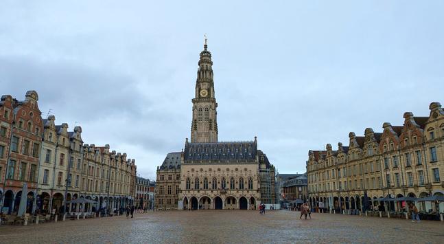 the Place des Heroes, at the town of Arras, Artois region, France. January 2025. In the centre is the town hall with its belfry. Just a couple of hours before this picture the square was a bustling market full of stalls and vehicles and Saturday shoppers. They were all gone and the square cleaned up by 2pm. The sides of the square are lined by homes with Flemish Baroque style gables, and there are many shops selling fries (Vlaams Fritjes) and of course the local beers and chocolates and despite being in France, many Flemish voices can be heard on the streets.