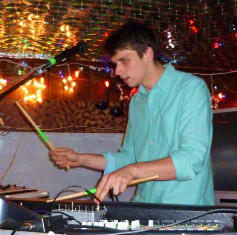 Brothertiger presses button on a synth board while holding two drum sticks.