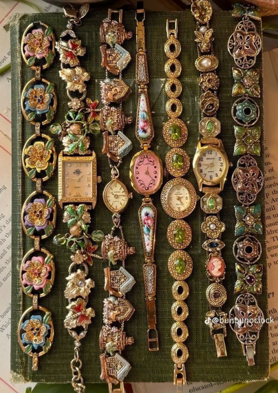 A vibrant collection of vintage watches and bracelets displayed on a dark green fabric background. Each piece features intricate designs, including floral motifs, gemstones, enamel detailing, and ornate patterns. The watches and bracelets showcase a mix of gold, silver, and colorful accents, exuding a timeless and luxurious aesthetic. A watermark reading "@bunbunjclock" is visible in the lower right corner.