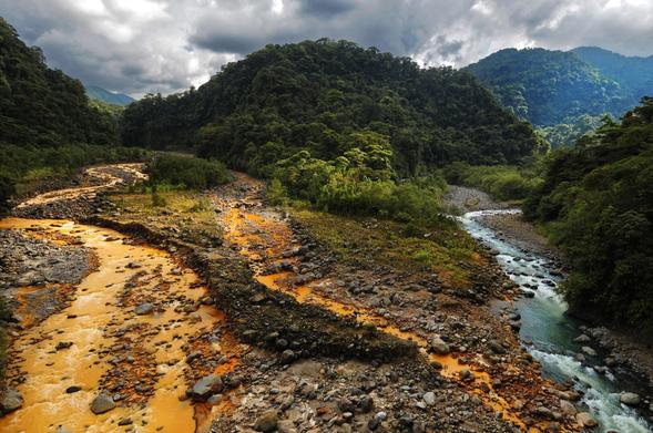 It's a picture of a river very spectacular : the Rio Sucio in Costa Rica. One side is almost rust color the other side is turquoise, blue. It's surrounded by mountains with dark clouds above.