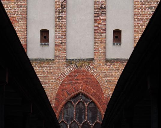 The east gable of a high medieval hospital church with two covered passageways from the Baroque period, through which the elderly and unfortunate could access a gallery in the church. Hatches and pointed arches form a face.