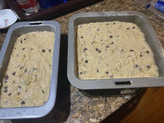 A loaf and a square cake pan filled with banana bread batter dotted with choc chips. They're sitting on the kitchen bench waiting for the oven.