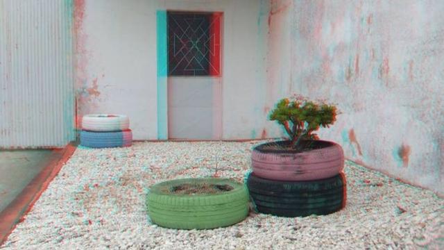 A red/cyan anaglyph of tyres turned into plant pots on a stony surface.