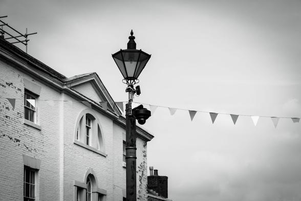 A lamppost in front of a building with some bunting attached against a cloudy sky.