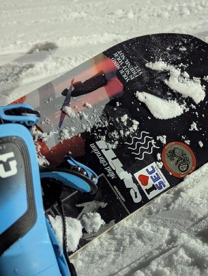 A snowboard with multiple stickers, covered slightly in snow. Also includes a GrrCON sticker as well as my own ilovesec sticker.