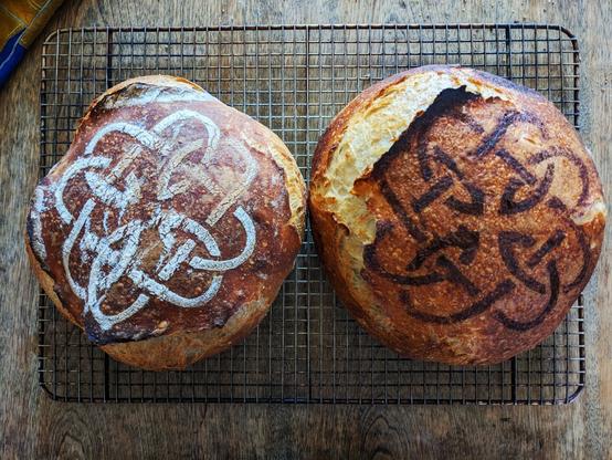 Two loaves of homemade "artisan" Rustic French (aka white) bread, shot from overhead. Each feature the same abstract stencil on top, one done in white rice flour, the other in brown cocoa powder. The image has been heavily filtered in the style of Instagram.