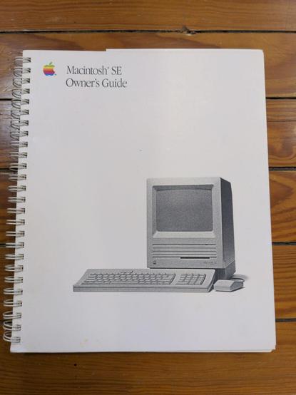 A spiral bound book lying on a wood floor. There is a six-color Apple logo in the upper left, next to Macintosh SE Owner's Guide in a serif font. A grayscale picture of a Macintosh SE with a single internal floppy drive and ADB extended keyboard and mouse takes up the bottom two thirds of the cover.