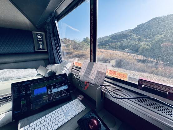 My mobile computer setup on a small desk next to a window showing the scenery passing by from inside a train.