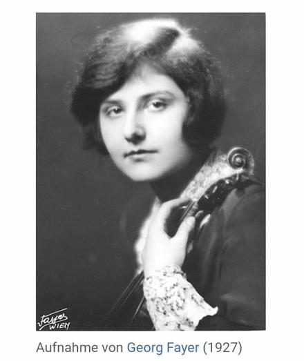 Schwarzweißporträt einer jungen Frau mit kurzen, welligen Haaren aus dem Jahr 1927. Sie trägt ein dunkles Oberteil mit Spitzenärmeln und hält eine Violine an ihrer Schulter. Der Fotograf ist Georg Fayer.