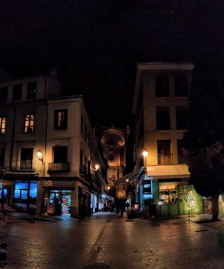 Vista nocturna de la calle Marqués de Gerona desde la plaza de la Pescadería. Al fondo de la calle se ve la plaza de las Pasiegas y la catedral. Los comercios de la calle están iluminados con luces de diferente color y la luz de la calle es amarilla.