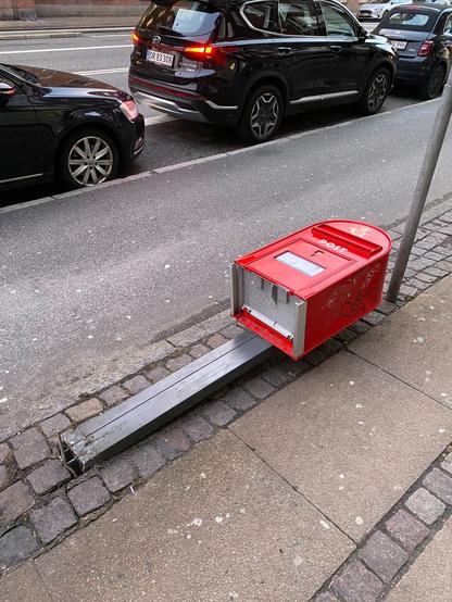 Danish red post box is literally laying down on the pavement due to someone have driven into it with a vehicle.