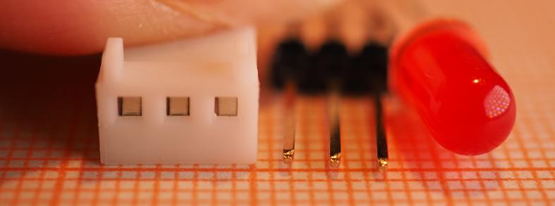 Electronic components, a white connector, a set of pins and a red LED on a graph paper