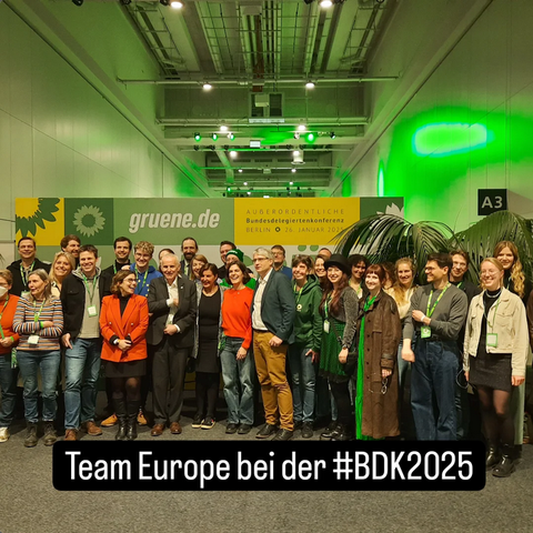Colourful group of over thirty people in front of a green banner
