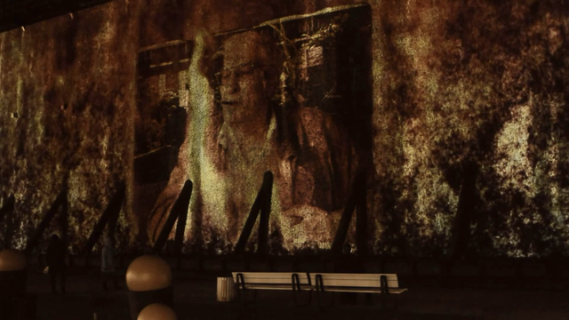 An giant artificial fire projection onto a saline wall made of blackthorn brushwood. Within the fire you can see a photo of a smoking man that is partially burnt.