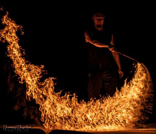 "A fire performer dressed in black, creating a dramatic arc of flames in the darkness with a fire staff."