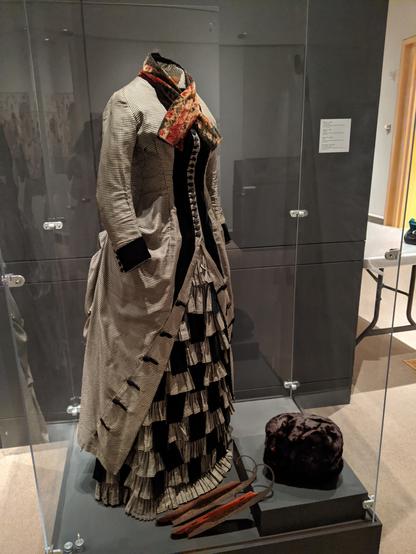 A day dress of black and white checked wool trimmed with black silk velvet, with a sable muff, orange scarf, and pair of skates.