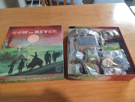 Photo of the board game "Now or Never" with the top cover off showing all of the components bagged and fitting inside the box.