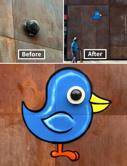 A dome-shaped security camera sticks out from the wall. The artist has painted a cute little blue cartoon bird around it, with the camera serving as the eye of the bird.