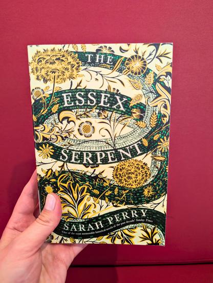 Holding the novel "The Essex Serpent" by Sarah Perry in front of a red background