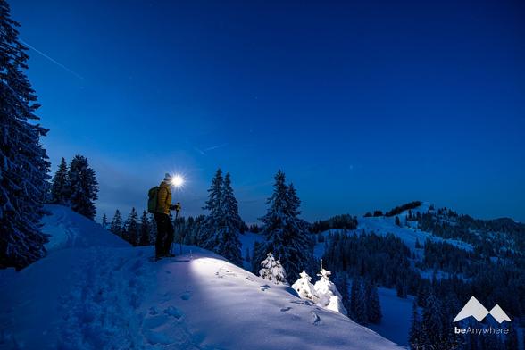 Person with a head lamp standing in the dark in a snowy landscape.