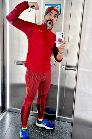 Fotografía en color frente al espejo de un ascensor. Llevo ropa de deporte ajustada roja y hago el gesto de flex como si fuera un gymbro